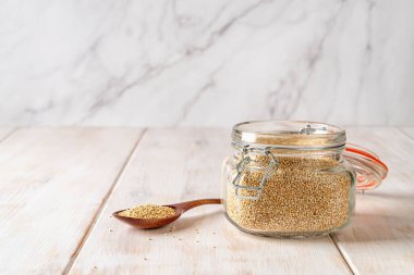 Kaşık içinde beyaz kinoa tohumları ve beyaz ahşap bir masada üst cam kavanozu klipslemek. Vejetaryen sağlıklı beslenmesi için çiğ kinoa pişiriyorum. Glütensiz yemekler için Chenopodium kinoası. Uzayı kopyala Ön görünüm.