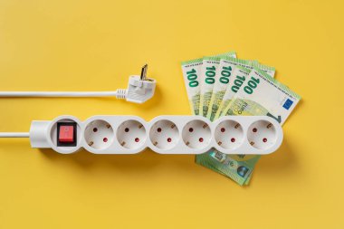 100 avro banknotta beyaz elektrik şeridi ve sarı arka planda beyaz elektrik prizi. Enerji krizinden dolayı artan enerji maliyetleri. Aydınlatma, ısıtma ve soğutma maliyetleri artarken enflasyon. Üst görünüm.