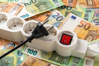 Switched off white power strip and unplugged black electric plug over euro banknotes background. Inflation and power crisis concepts. Increasing the energy costs, save electricity. Top view.