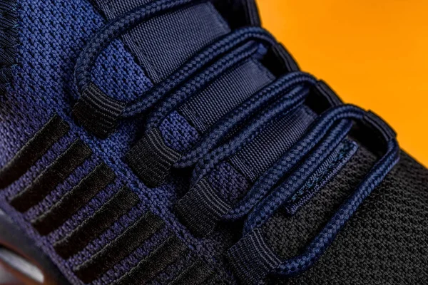 Laced up fastening of new sport shoe against orange background. Lacing of black blue mesh fabric sneakers macro. Modern textile sneakers with elastic laces for active lifestyle, sports and fitness. Close-up.