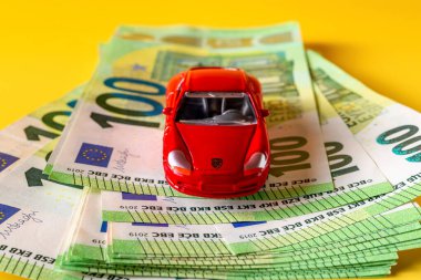 Varna, Bulgaristan, 10 Mayıs 2022. 100 avroluk banknotların üzerinde kırmızı Porsche minyatür araba modeli. Otomobil sigortası ve otomobil kredisi kavramları. Araba yatırımı, para, servet. Ön görünüm.