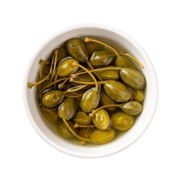 Beyaz arka planda izole edilmiş beyaz bir kasede turşu üzümü. Kapari çalılarının marine edilmiş meyveleri. Baharat ve garnitür olarak konserve yaban mersini. Akdeniz mutfağının ortak bileşeni. Üst görünüm.