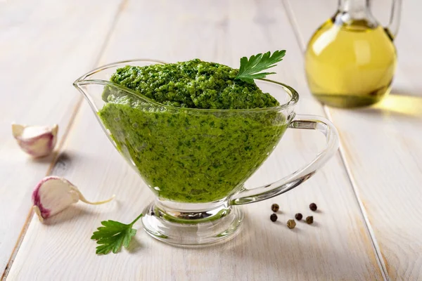 Green sauce in a gravy boat on a table. Chimichurri dipping sauce from fresh parsley, garlic cloves, olive oil and lemon juice. Salsa verde with fresh herb and spices. Healthy condiment. Close-up.