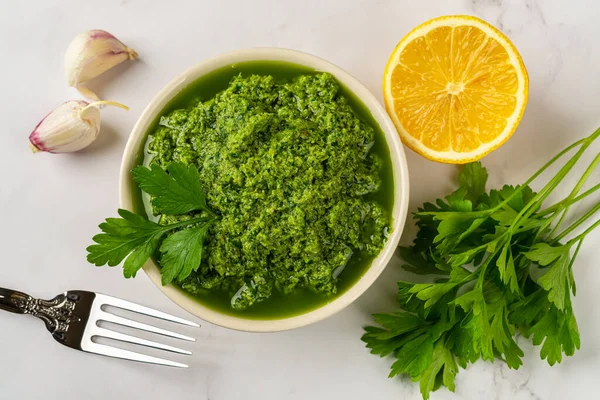 Fresh salsa verde in a bowl. Chimichurri dipping sauce from fresh parsley, garlic cloves, olive oil and lemon juice. Green sauce with fresh herb and spices. Healthy condiment recipe. Top view.