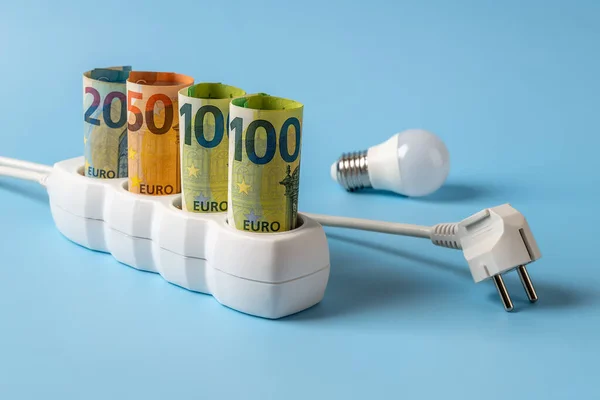 Energy price spike. Rising of electricity bill payment. Euro banknotes plugged into electrical outlet, light bulb and white power plug against blue background. High energy costs in Europe. Front view.