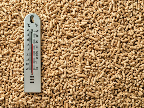 Air thermometer over wood pellets background. Ecological home heating with organic biofuel from compressed sawdust. Alternative renewable energy, bio fuel concept. Copy space. Top view.