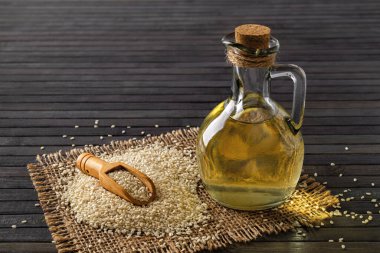 Fresh sesame oil in a glass jug and heap of white til seeds over black background. Vegetable oil from Sesamum indicum. Organic benne seeds for boosting immunity diet and calcium source. Front view.