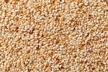 Roasted sesame seeds macro background. Texture of toasted Sesamum indicum closeup. Organic benne seeds as asian cuisine ingredient. White til as calcium source for healthy food concept. Top view.