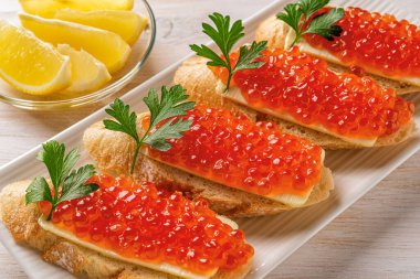Sandwiches with red caviar on a white plate. Gourmet appetizer of trout caviar on a slice of french baguette with butter. Salted salmon roe for seafood fish delicacy concept. Front view.