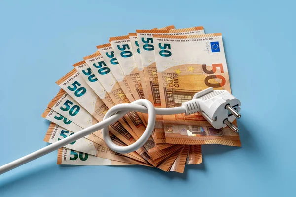 Knotted power cable with electric plug on fan shaped 50 euro banknotes over blue background. Soaring of electricity prices in Europe. Energy price spike. Rising energy costs. Top view.