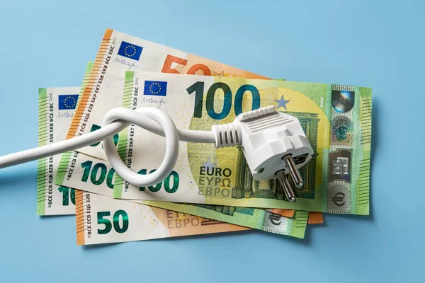 Knotted power cable with electric plug on 50 and 100 euro banknotes over blue background. Concept of rising energy costs in Europe. Electric bill increases. Power price spike. Top view.