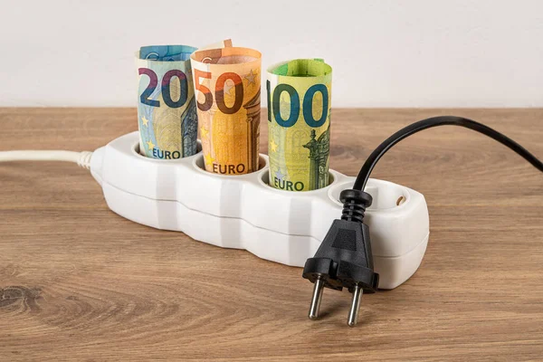 Unplugged electric plug at power strip with rolled euro currency banknotes on a floor. Electric bill increases in Europe. Energy price spike. Soaring of electricity prices. Front view.