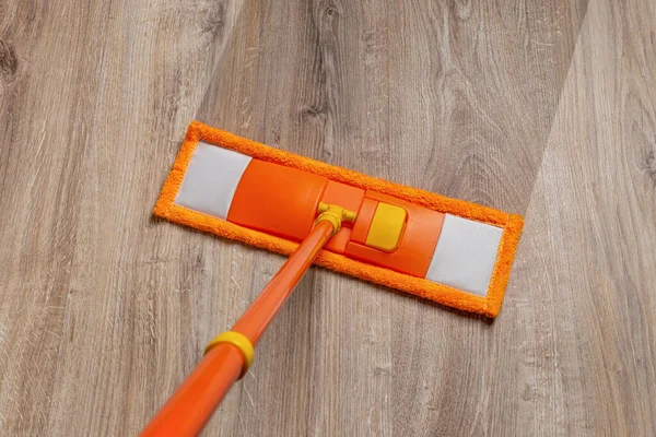 Orange mop washing dusty floor at home. Cleaning the wooden laminate floor with wet microfiber mop. Mopping the floor. Housekeeping, homework routine, cleaning concept. Top view.