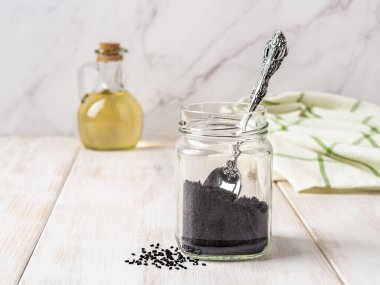 Beyaz ahşap bir tezgahta cam bir kavanozda kurutulmuş nigella tohumları ve kaşık. Pişirmek için siyah kimyon kullanıyor. Baharat ve baharat konsepti için Kalonji. Ayurvedic şifalı bitki nigella sativa. Ön görünüm.