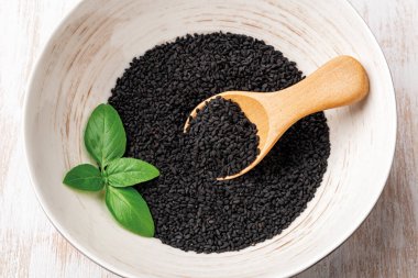Siyah kimyon tohumları ve beyaz kasede tahta kaşık. Pişirmek için kalonji kuru tohumu kullanıyorum. Organik baharat ve baharat kavramı. Nigella sativa bitkisel ilaçlar ve Ayurveda için. Üst görünüm.