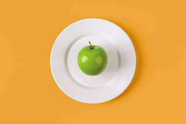 Sarı arka planda beyaz bir tabakta organik yeşil elma. Antioksidan için organik bileşenler sağlıklı beslenir. Zayıflatmak için taze meyve. Vitamin vejetaryen atıştırmalığı. Üst görünüm.