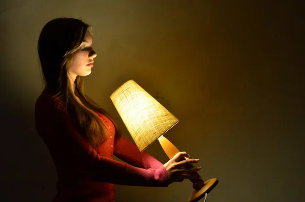 The girl is holding in the hands of the lamp and looks at her — Stock Photo, Image