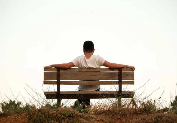 alone young man sitting on bench, back view. thinking or hope or loneliness or leisure or rest concept. selective focus