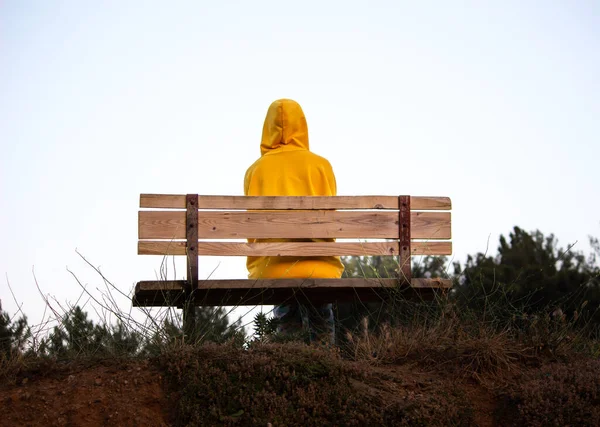 A lonely young person sits on a bench. wearing a yellow hoodie. selective focus include.