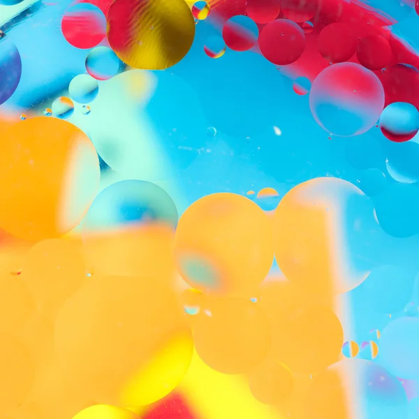 Gotas de aceite en el agua sobre un fondo coloreado — Foto de Stock