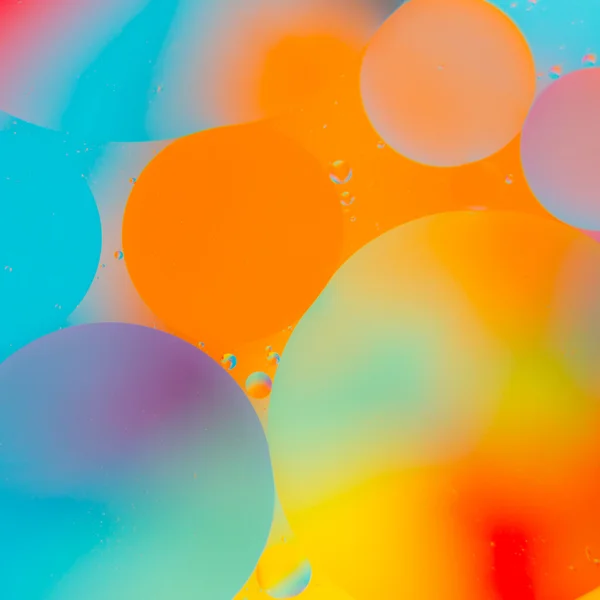 Olja droppar i vatten på en färgad bakgrund — Stockfoto