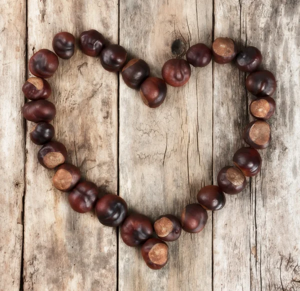 Chestnuts forming a heart on a wooden background — Stock Photo, Image