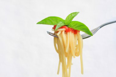 Domates soslu spagetti ve çatala sarılmış fesleğen.
