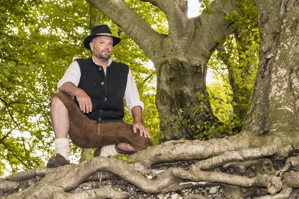 Kneeling man in traditional Bavarian costumes in forest — Stock Photo, Image