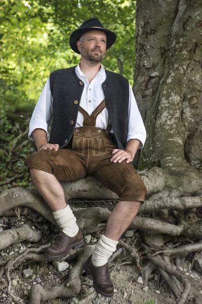 Hombre sentado en trajes tradicionales bávaros en el bosque —  Fotos de Stock