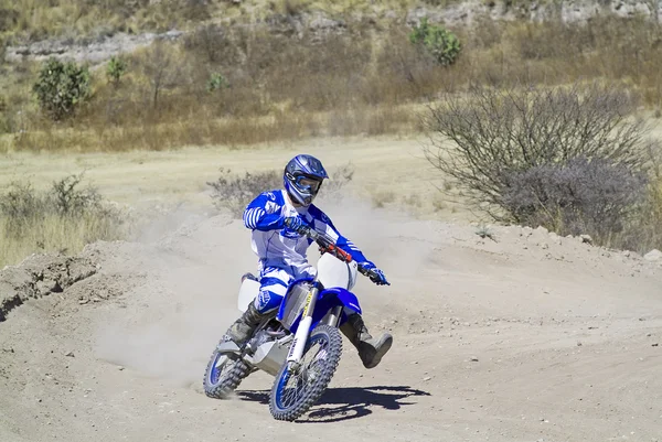 Föraren går sluttande lämnar ett spår av damm med sin motocross cykel — Stockfoto