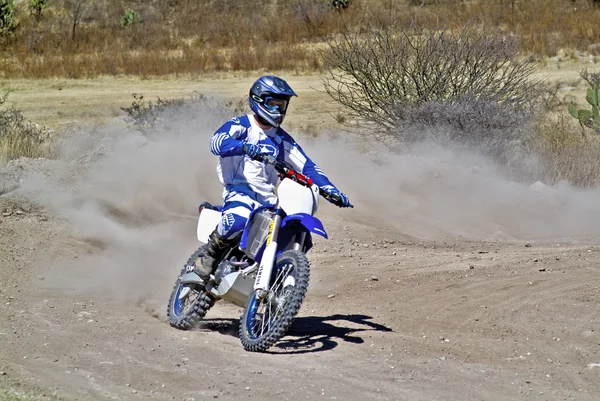 Driver goes downhill leaving a trail of dust with his motocross bike — Stock Photo, Image