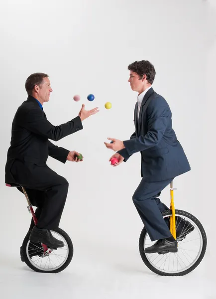 Żonglerka biznesmenów jazda rowerów jednokołowych Obrazek Stockowy
