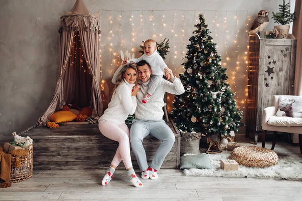 Hermosa familia joven jugar con su hijo pequeño en una habitación con un árbol de Navidad —  Fotos de Stock