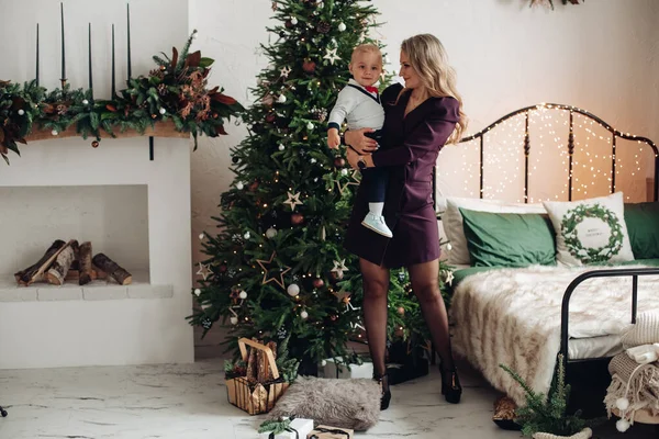 Madre caucásica sostiene a su encantadora hija en las manos cerca del árbol de Navidad —  Fotos de Stock