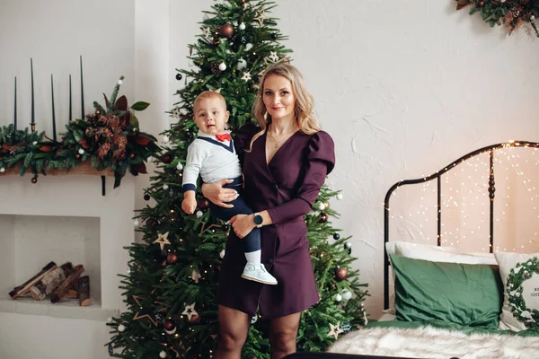 Kaukasische moeder houdt haar mooie dochter op de handen in de buurt van de kerstboom thuis — Stockfoto