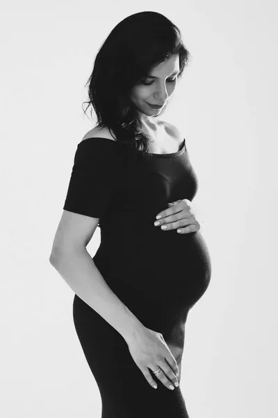 Frumoasă femeie gravidă tânără îmbrățișând burta pozând în studio, fotografie alb-negru. Sarcina fericită și maternitatea — Fotografie, imagine de stoc