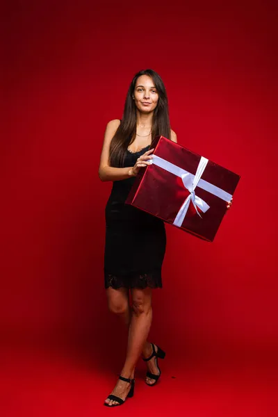 Щаслива брюнетка з червоною подарунковою коробкою позує в студії — стокове фото