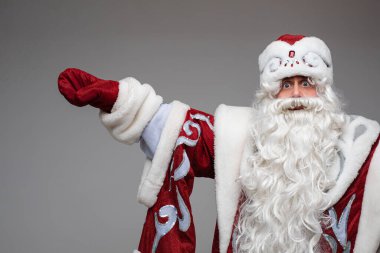 Noel Baba, gri stüdyo arka planında boş bir alanı işaret ediyor. Yeni yıl reklamı için fotokopi alanı var.