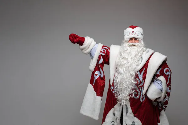 산타 클로스는 크리스마스 신년 광고 사본을 위한 공간을 회색 스튜디오 배경으로 빈 공간에 손으로 가리키고 있다 — 스톡 사진
