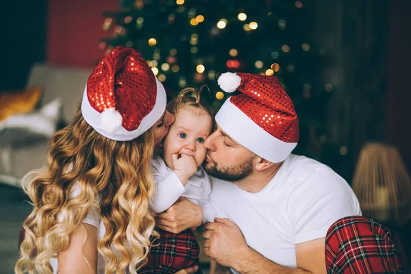 Rodiče v Santa klobouky líbání dítě. — Stock fotografie