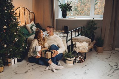 Erkek ve kadın, Noel ağacının yanındaki yatak odalarında yerde oturuyorlar.