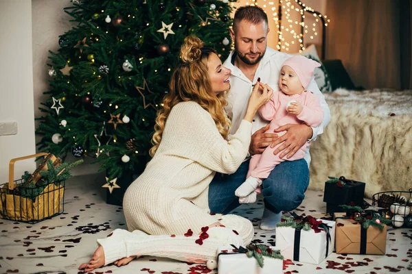 Sonriente padre y madre mirando a su lindo bebé cerca del árbol de Navidad —  Fotos de Stock