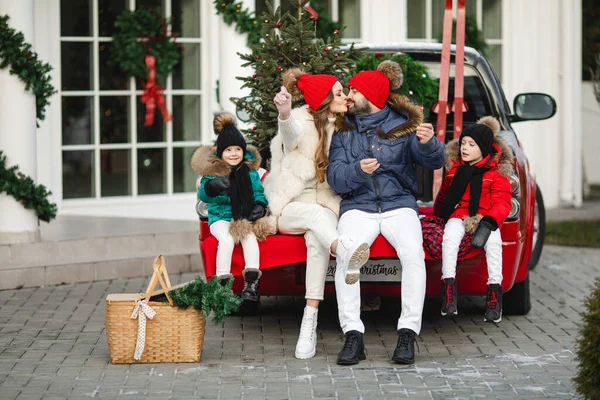 행복 한 가족은 크리스마스 이브에 집 근처의 붉은 차에 앉아 있다 — 스톡 사진
