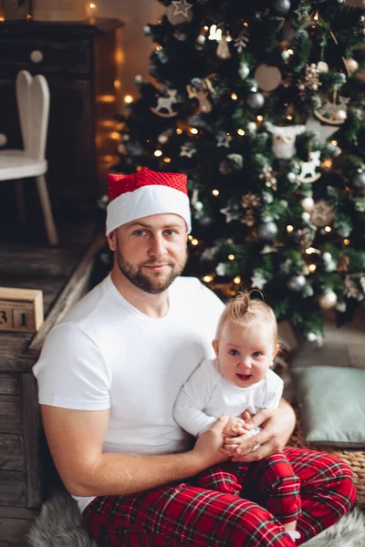 Sonriente hombre en sombrero de Santa sentado con su hijo en el suelo en casa —  Fotos de Stock