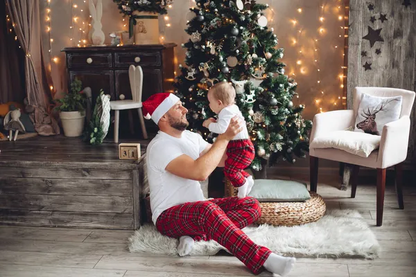 Guapo padre joven sostiene a un bebé cerca del árbol de Navidad —  Fotos de Stock