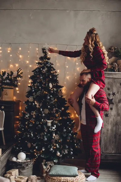 Esposa decora árbol de Navidad con su marido en la misma ropa de dormir juntos en casa — Foto de Stock