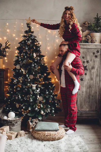 Smiling man holding beautiful wife on his shoulders on Christmas eve — Stock Photo, Image