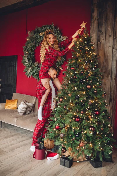 Cuplu vesel în dragoste în aceeași lenjerie de somn decorează pomul de Crăciun împreună — Fotografie, imagine de stoc