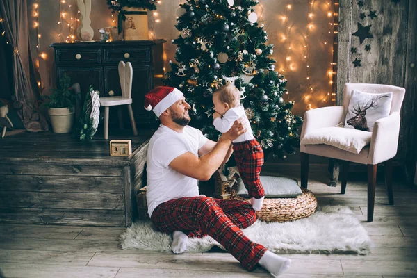 Hombre sonriente sosteniendo a su bebé mientras juega cerca del árbol de Navidad —  Fotos de Stock