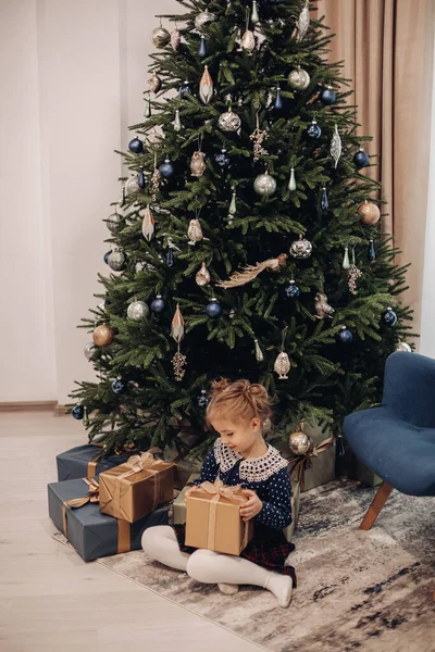 Pequeña chica caucásica mira su cintura cerca del árbol de Navidad en casa — Foto de Stock